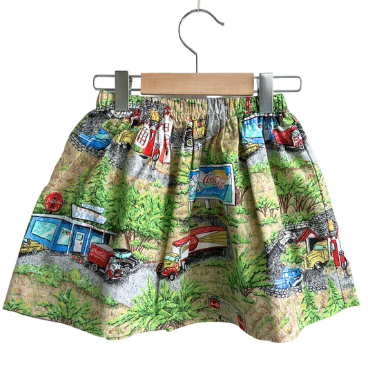Skirt with vintage truck and car print on a hanger against a white background